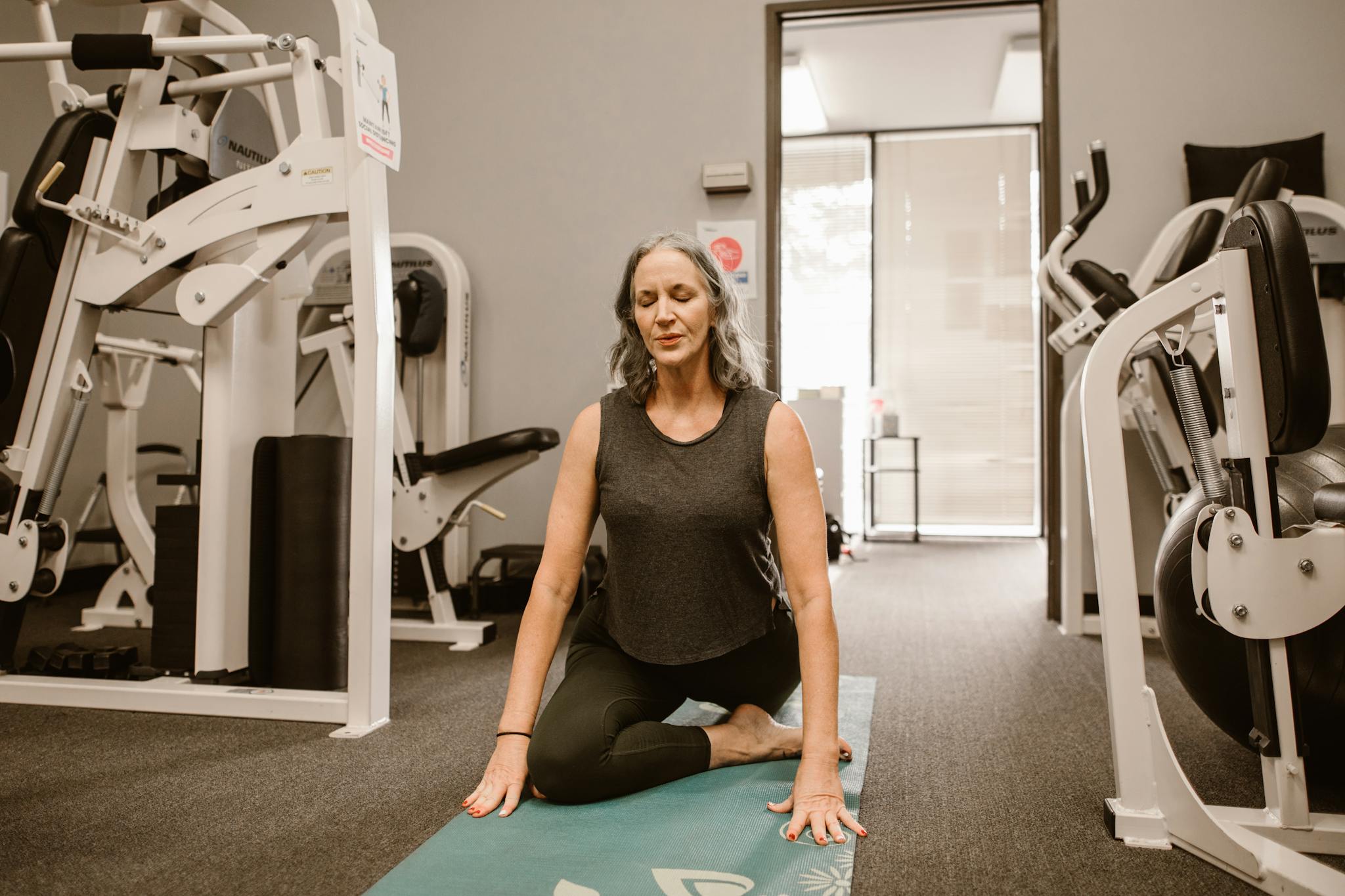 A midlife woman meditates on a yoga mat in a gym, practicing mindfulness and wellness.