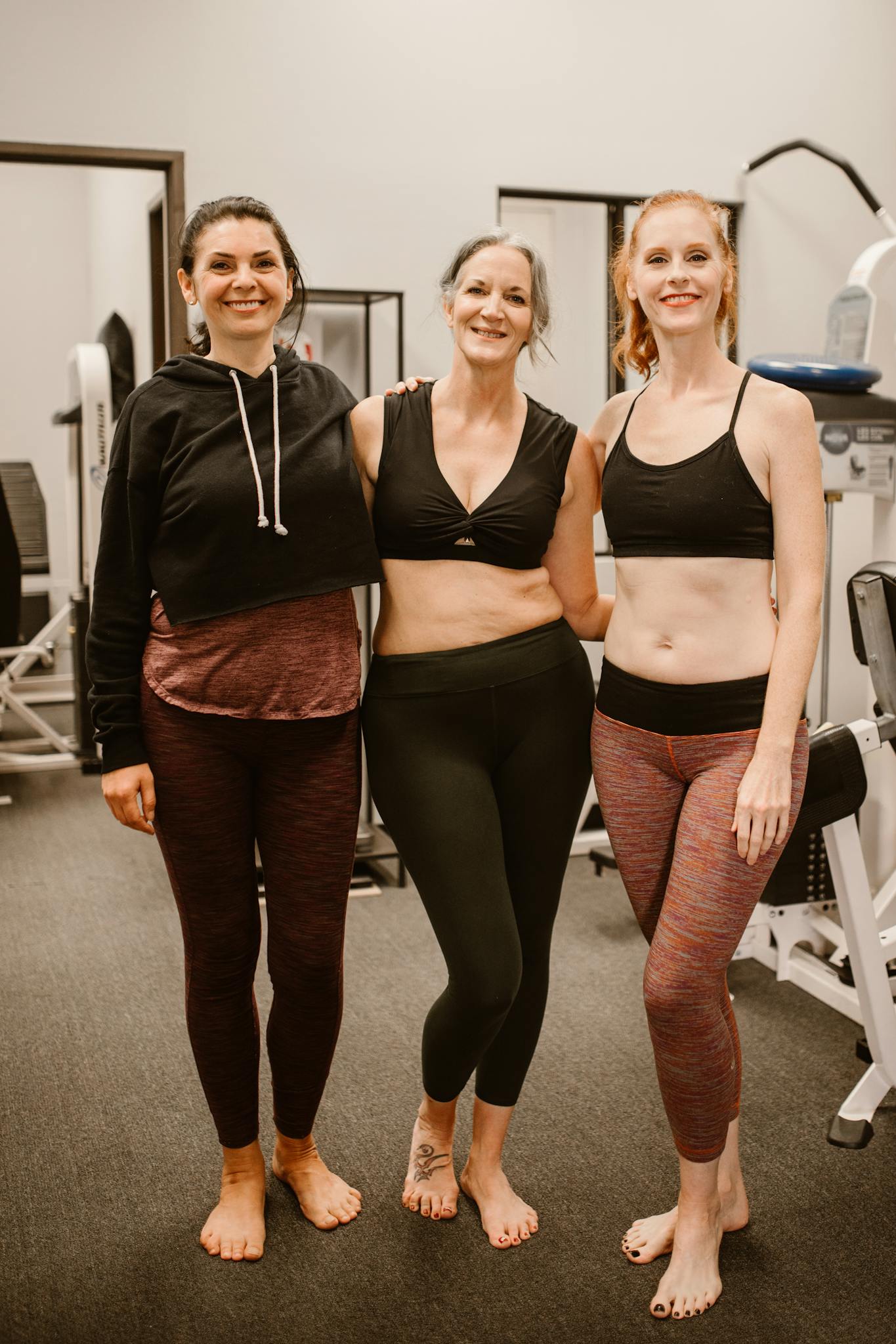 Three diverse women in athletic wear smiling confidently in a gym setting.